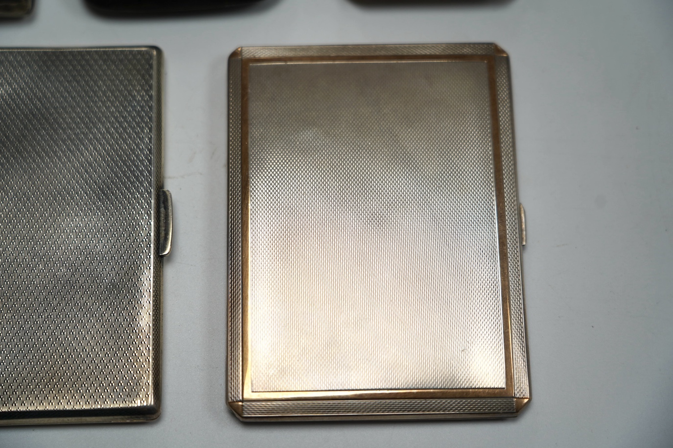 A George VI engine turned silver cigarette case, with yellow metal band, London, 1938, 11.4cm, four other silver cigarette cases and a silver ashtray, gross weight 16.8oz. Condition - poor to fair